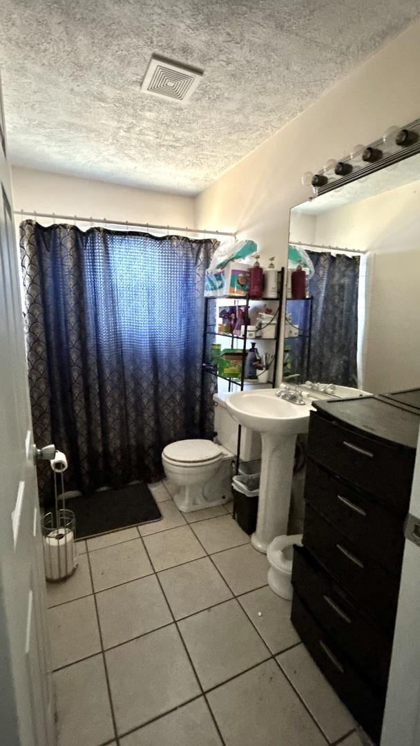 bathroom with toilet, visible vents, a textured ceiling, and tile patterned floors