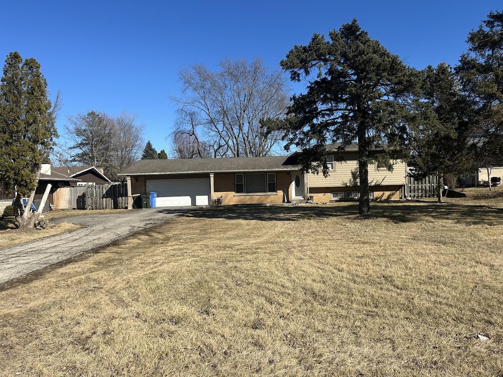 tri-level home featuring a front lawn, dirt driveway, an attached garage, and fence