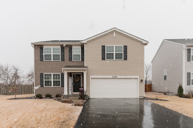 traditional home with an attached garage, fence, and aphalt driveway