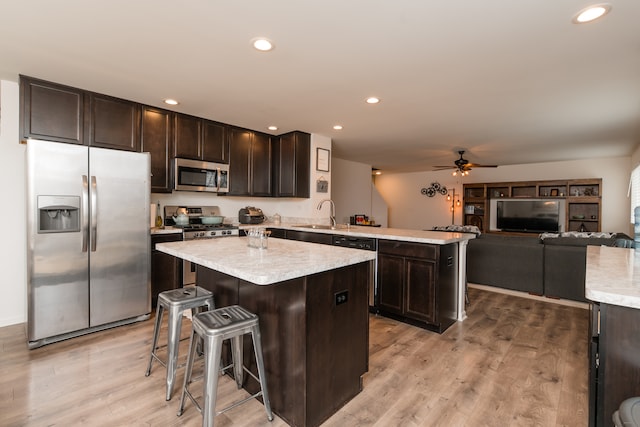 kitchen featuring stainless steel appliances, light wood-type flooring, dark brown cabinetry, and a peninsula