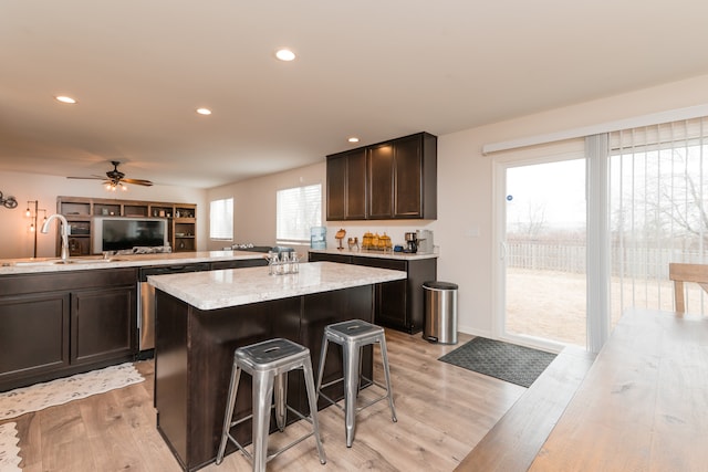 kitchen featuring dark brown cabinetry, light wood-style flooring, a kitchen breakfast bar, a center island, and a sink