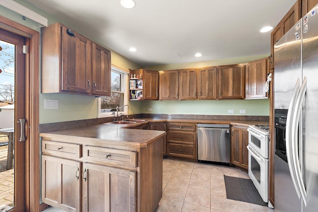 kitchen featuring a sink, dark countertops, appliances with stainless steel finishes, a peninsula, and light tile patterned floors