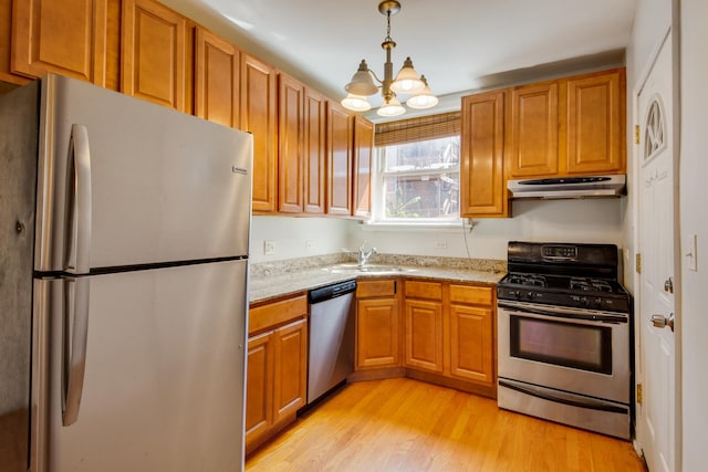 kitchen featuring light wood finished floors, a sink, under cabinet range hood, appliances with stainless steel finishes, and a chandelier