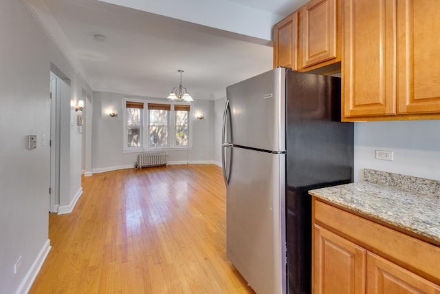 kitchen featuring light wood-type flooring, a notable chandelier, light stone counters, freestanding refrigerator, and radiator