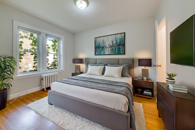 bedroom with baseboards, radiator heating unit, and light wood finished floors