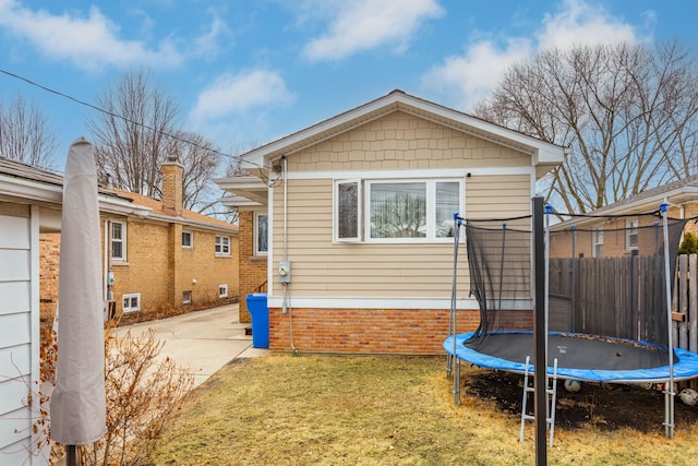 back of property with a trampoline, fence, and a lawn