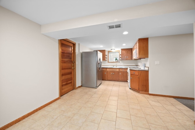 kitchen featuring white appliances, visible vents, baseboards, light countertops, and brown cabinetry