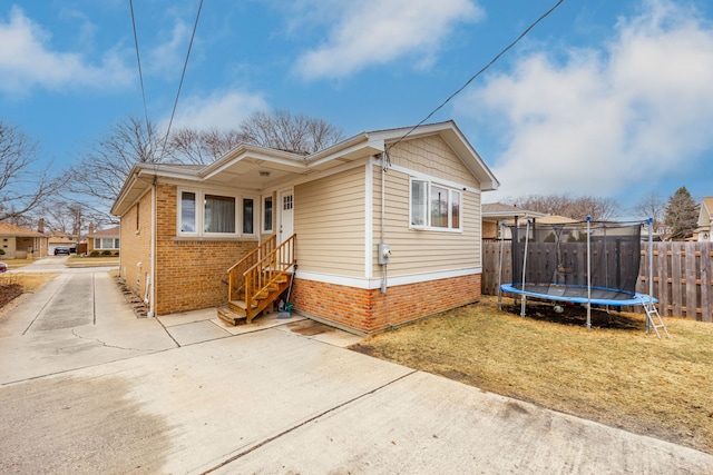 view of front of house featuring a trampoline, brick siding, and fence