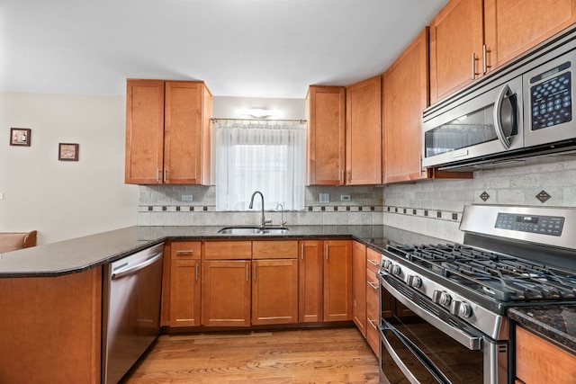 kitchen with light wood finished floors, tasteful backsplash, a peninsula, stainless steel appliances, and a sink