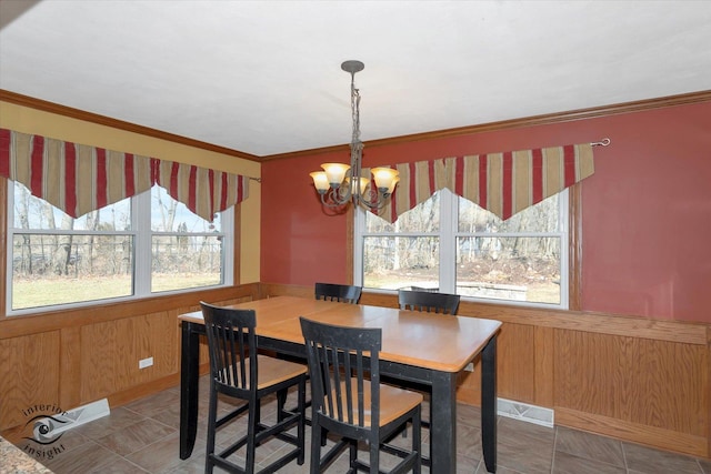 dining space featuring a chandelier, wooden walls, wainscoting, and crown molding