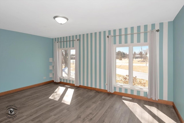 spare room featuring visible vents, wallpapered walls, baseboards, and wood finished floors