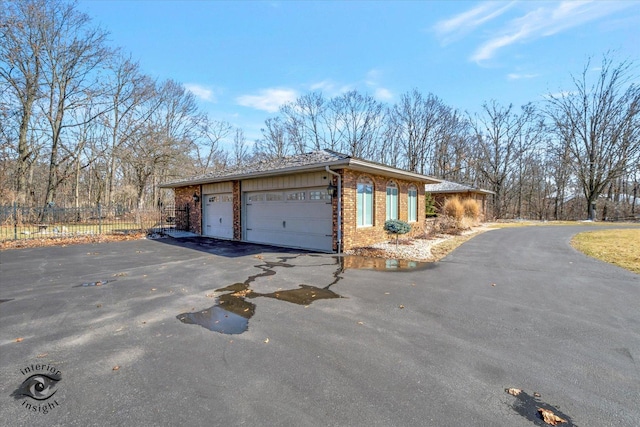 view of side of property with a garage, fence, brick siding, and driveway