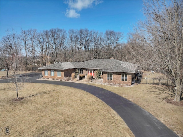 view of front of property featuring aphalt driveway, brick siding, a front lawn, and fence