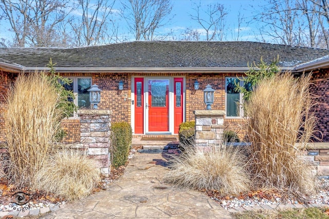 view of exterior entry featuring brick siding and roof with shingles