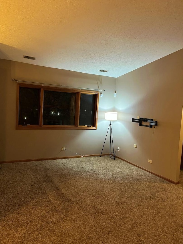 empty room featuring carpet, visible vents, a textured ceiling, and baseboards