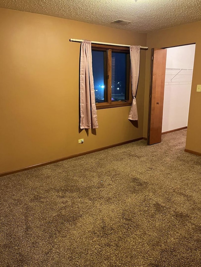 carpeted spare room featuring a textured ceiling and baseboards