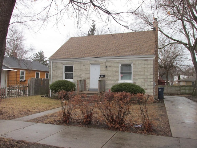 bungalow with a shingled roof, a chimney, and fence