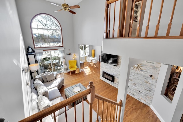 living area featuring a high ceiling, a ceiling fan, wood finished floors, and a stone fireplace