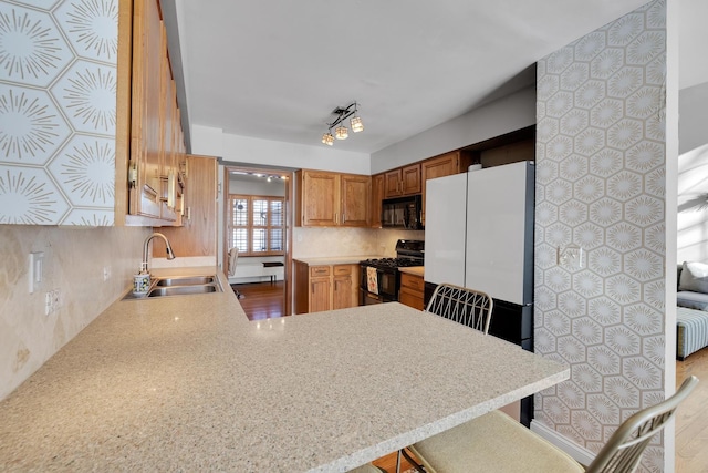 kitchen with tasteful backsplash, light countertops, a sink, a peninsula, and black appliances