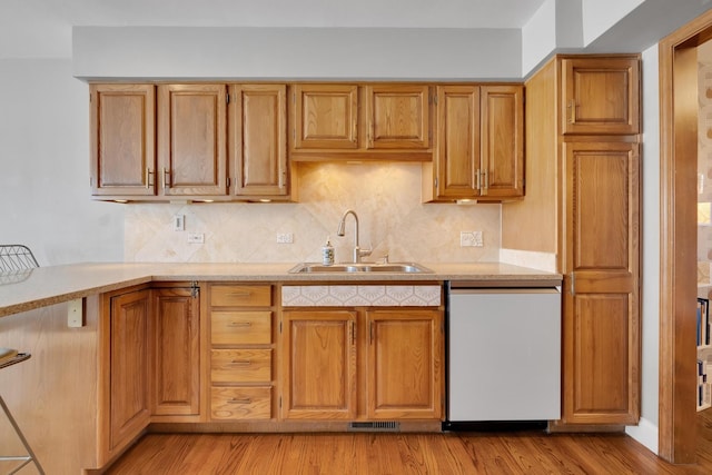 kitchen with decorative backsplash, brown cabinets, white dishwasher, light wood-type flooring, and a sink