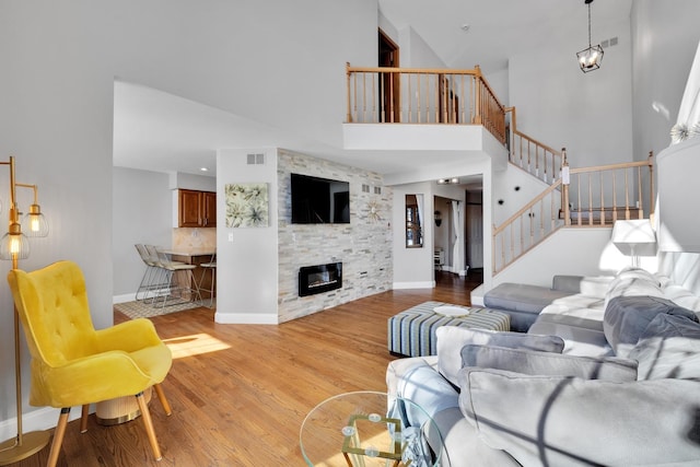 living area featuring a stone fireplace, visible vents, baseboards, light wood-style floors, and stairway