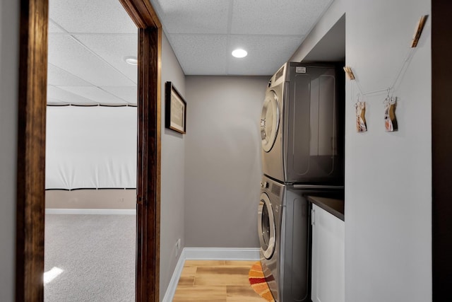 laundry room featuring light wood-style floors, stacked washer / dryer, and baseboards