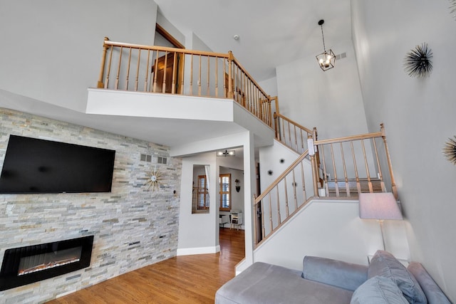 living room featuring a stone fireplace, stairway, wood finished floors, and a towering ceiling