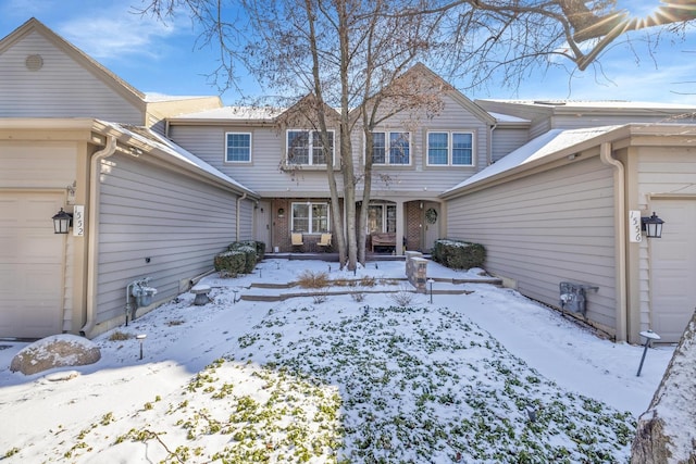 snow covered rear of property with brick siding and an attached garage