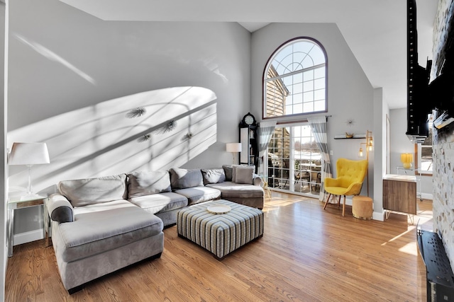 living area with a towering ceiling, baseboards, and wood finished floors