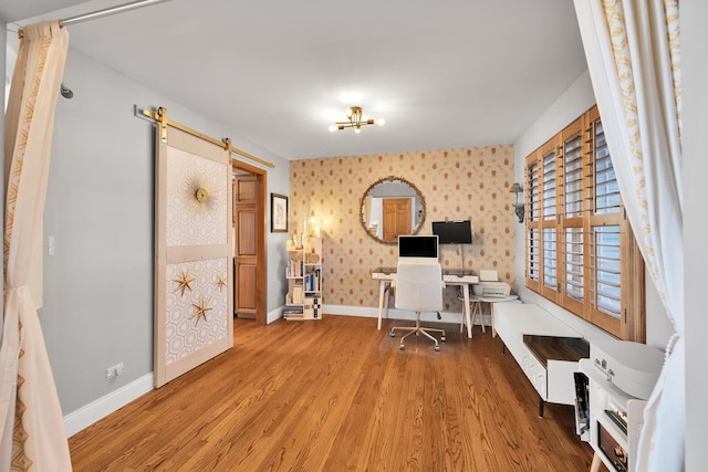 office with light wood-type flooring, wallpapered walls, a barn door, and baseboards