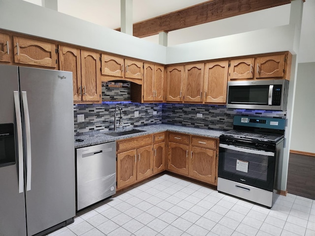 kitchen featuring stainless steel appliances, tasteful backsplash, brown cabinetry, a sink, and beamed ceiling