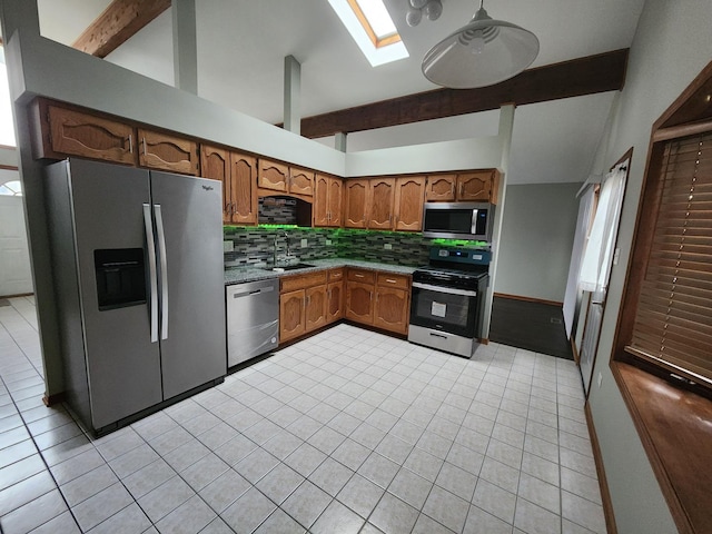 kitchen featuring appliances with stainless steel finishes, vaulted ceiling with skylight, a sink, and decorative backsplash