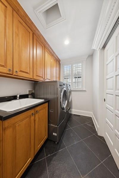 washroom with attic access, dark tile patterned flooring, cabinet space, a sink, and washer and dryer