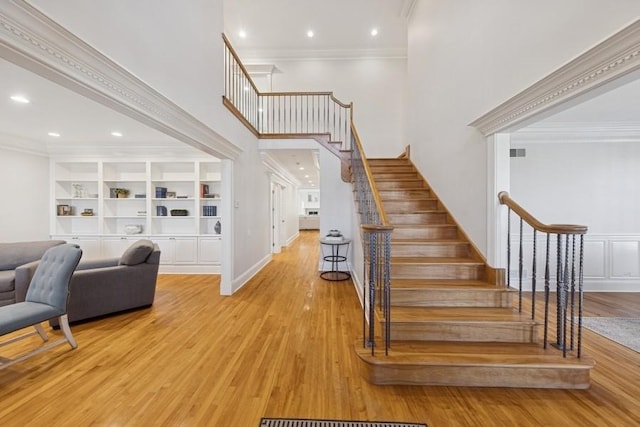 stairway with crown molding, a high ceiling, built in features, and wood finished floors