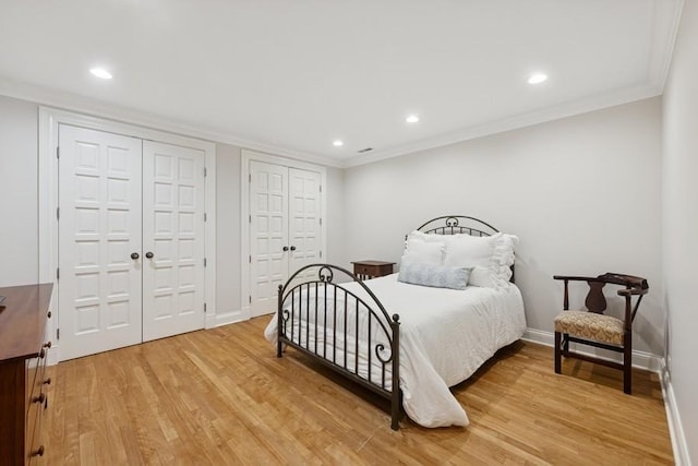 bedroom featuring two closets, ornamental molding, recessed lighting, light wood finished floors, and baseboards