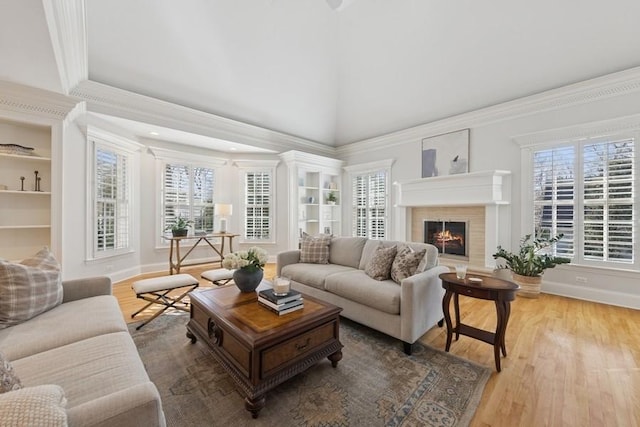 living room featuring built in features, wood finished floors, a lit fireplace, vaulted ceiling, and crown molding