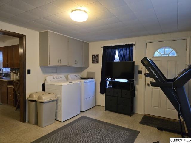 clothes washing area with cabinet space, washing machine and dryer, and light floors