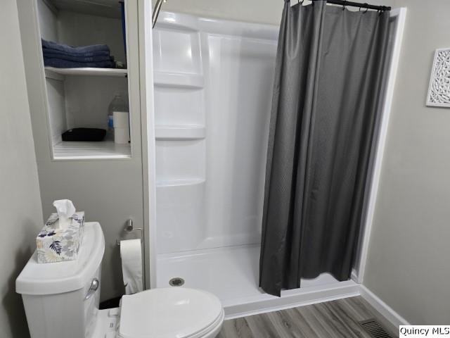 full bath featuring a stall shower, baseboards, visible vents, toilet, and wood finished floors