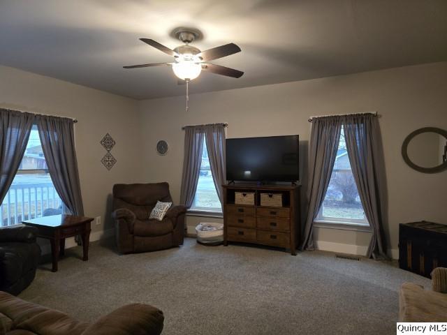 living area featuring a wealth of natural light, carpet, and ceiling fan