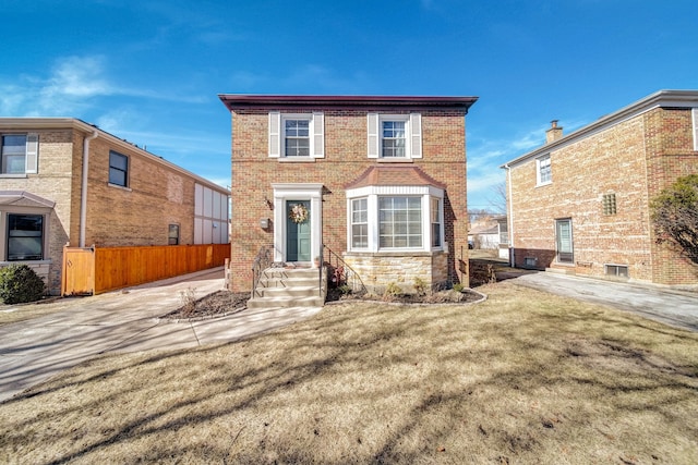 view of front facade with brick siding, a front yard, and fence