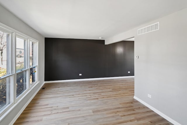 empty room with light wood finished floors, baseboards, and visible vents