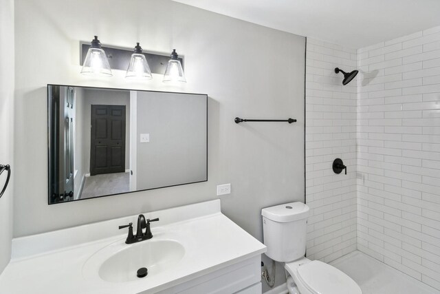 full bathroom featuring tiled shower, vanity, and toilet