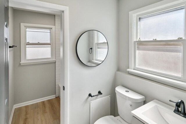 bathroom with a wealth of natural light, baseboards, toilet, and wood finished floors