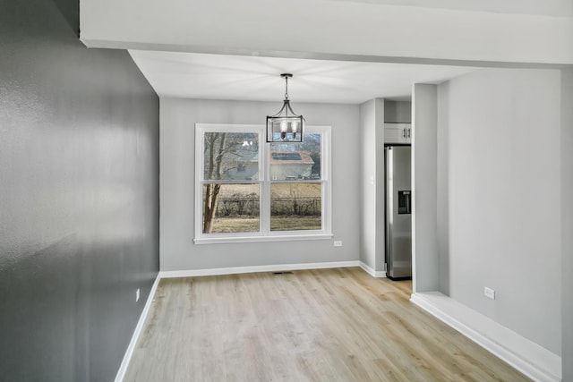 unfurnished dining area with a notable chandelier, light wood-style flooring, and baseboards