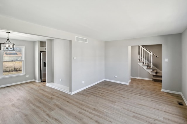 empty room featuring light wood-style floors, visible vents, and stairs