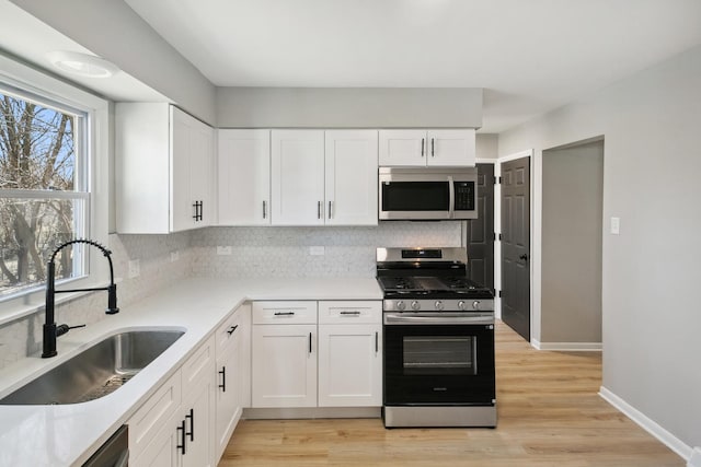 kitchen featuring stainless steel appliances, backsplash, a sink, and white cabinetry