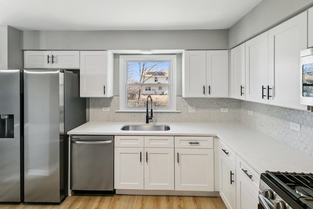 kitchen featuring light wood-style flooring, a sink, white cabinets, light countertops, and appliances with stainless steel finishes