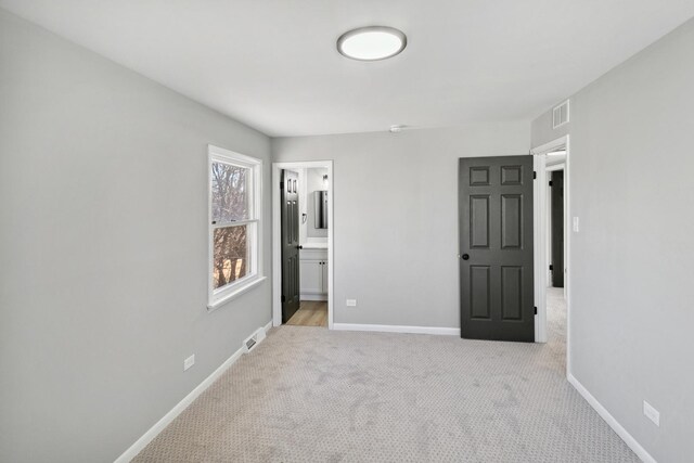 unfurnished bedroom with baseboards, ensuite bathroom, visible vents, and light colored carpet