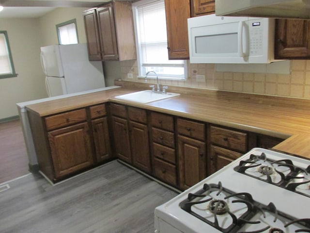 kitchen with white appliances, tasteful backsplash, a peninsula, light countertops, and a sink