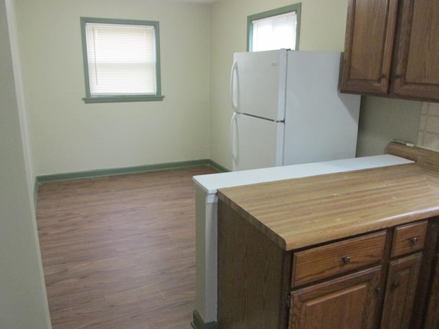 kitchen featuring a peninsula, wood finished floors, baseboards, light countertops, and freestanding refrigerator